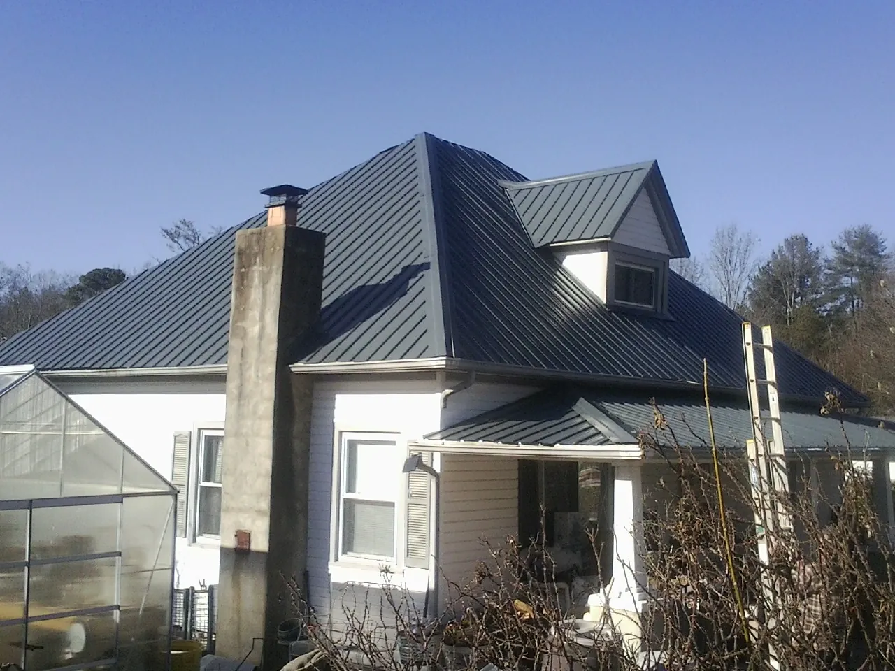 Dark blue standing seam metal roof on a white farmhouse with dormer — Slate & Tile Roof Repair by Roofing Brothers in Nancy