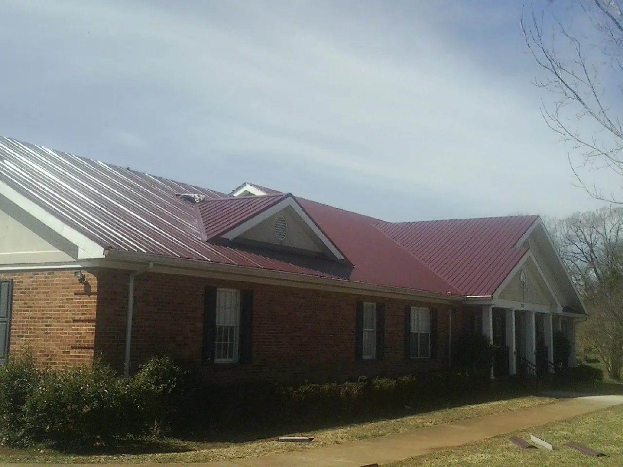 Red metal roof with gabled entries on a long brick building, from a Hail Damage Roof Repair job in Nancy