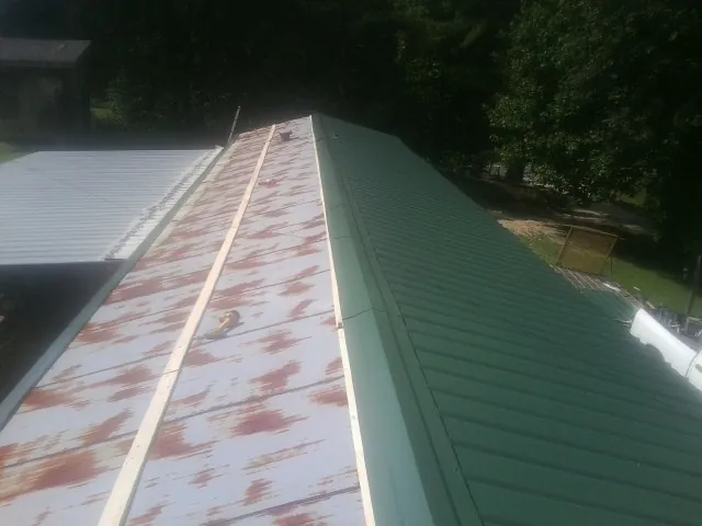 Old rusted panels beside newly installed green metal roofing — Wind Damage Roof Repair by Roofing Brothers in Nancy