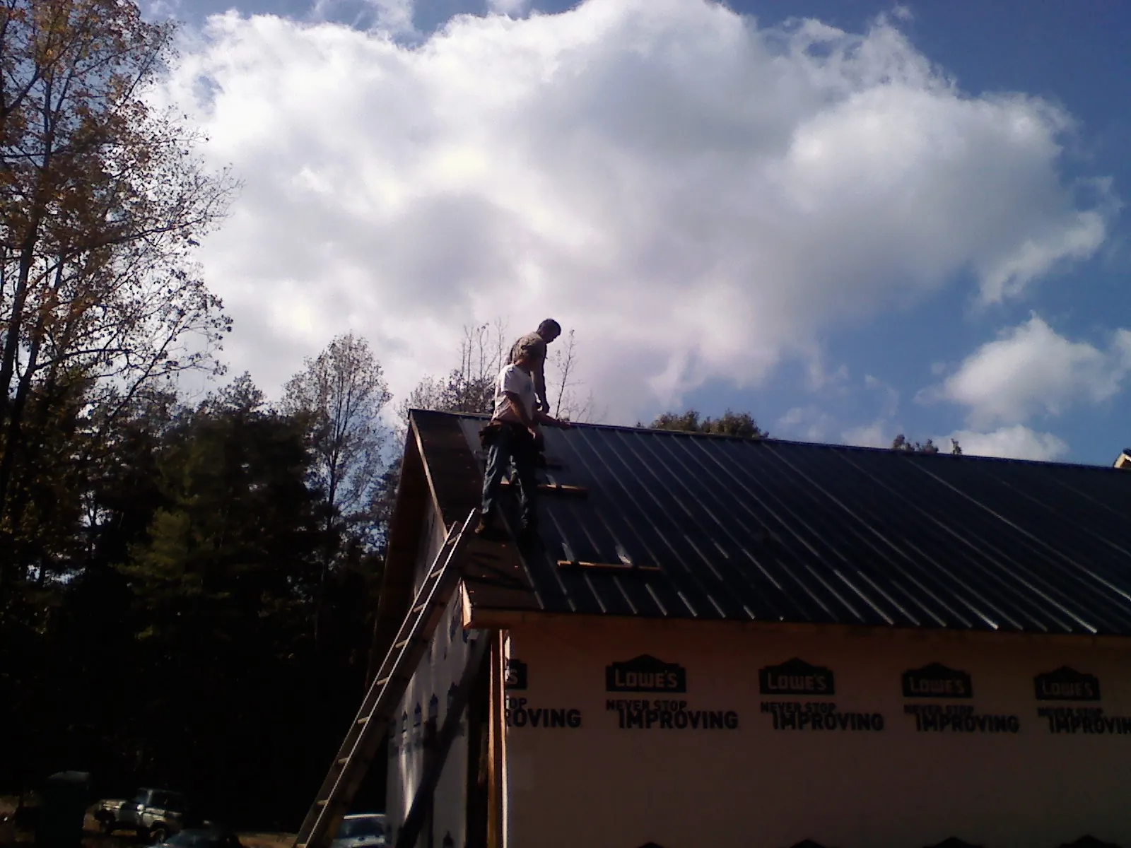 Roofer fastening dark metal panels high against a cloudy sky, from a Roof Inspection job in Nancy