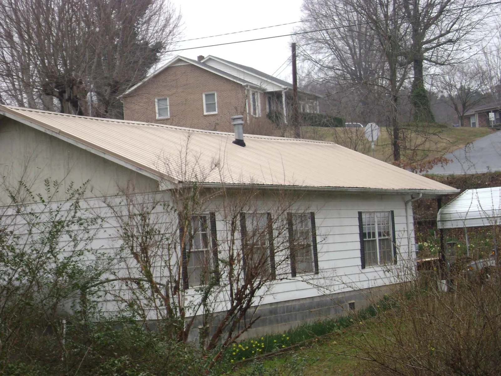 Tan metal roof on a white sided house set into a hillside — Commercial Roofing by Roofing Brothers in Nancy
