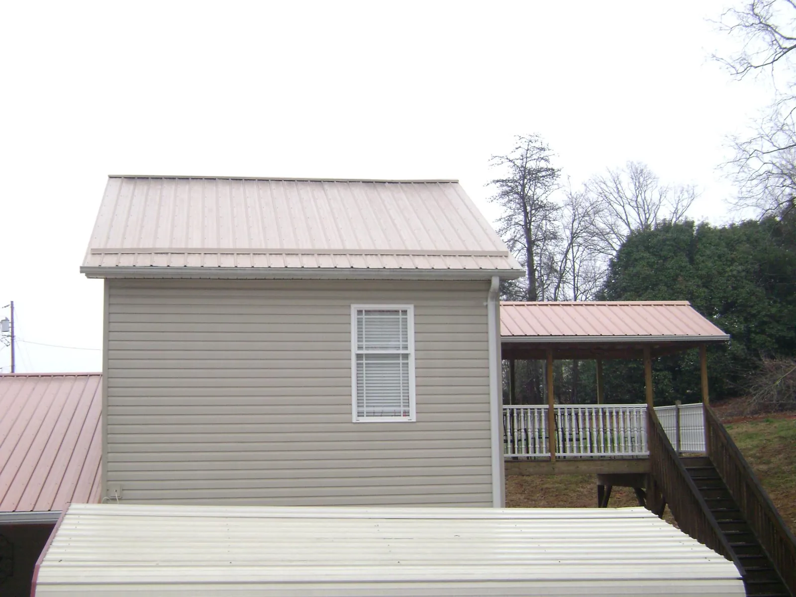 Tan metal roofs on a two story addition and attached porch, from a Roof Replacement job in Nancy